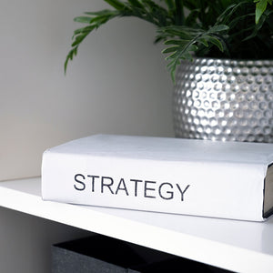 ספר עם הכיתוב STRATEGY ליד עציץ – חיבור בין חשיבה שיווקית לעיצוב חווייתי.
Strategy book beside a plant – representing the merge between business thinking and visual storytelling.